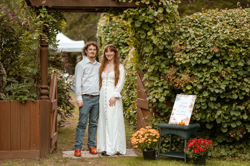 A couple stands in a garden archway decorated with autumn flowers and greenery.