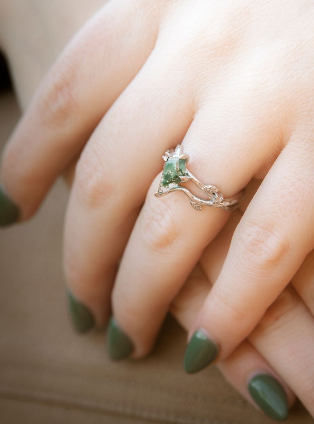 Close-up sequence showing a delicate silver ring with a small green gemstone being worn on a hand with sage green nails.