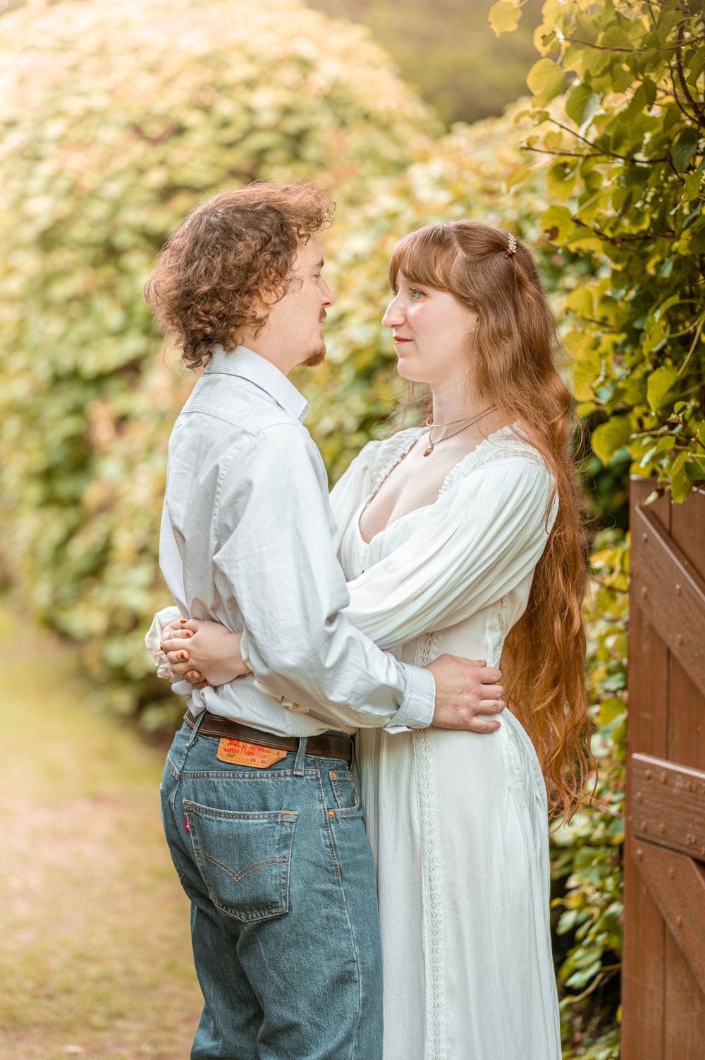 A romantic moment captured between a couple in white and casual attire against garden foliage.