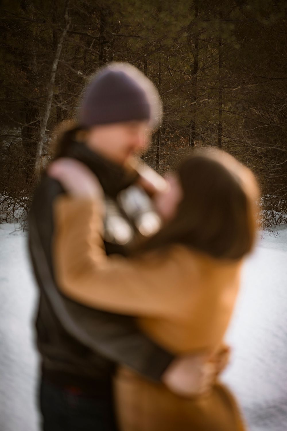 Blurred couple embracing in a snowy winter forest, wearing warm coats and hats in a romantic outdoor setting.