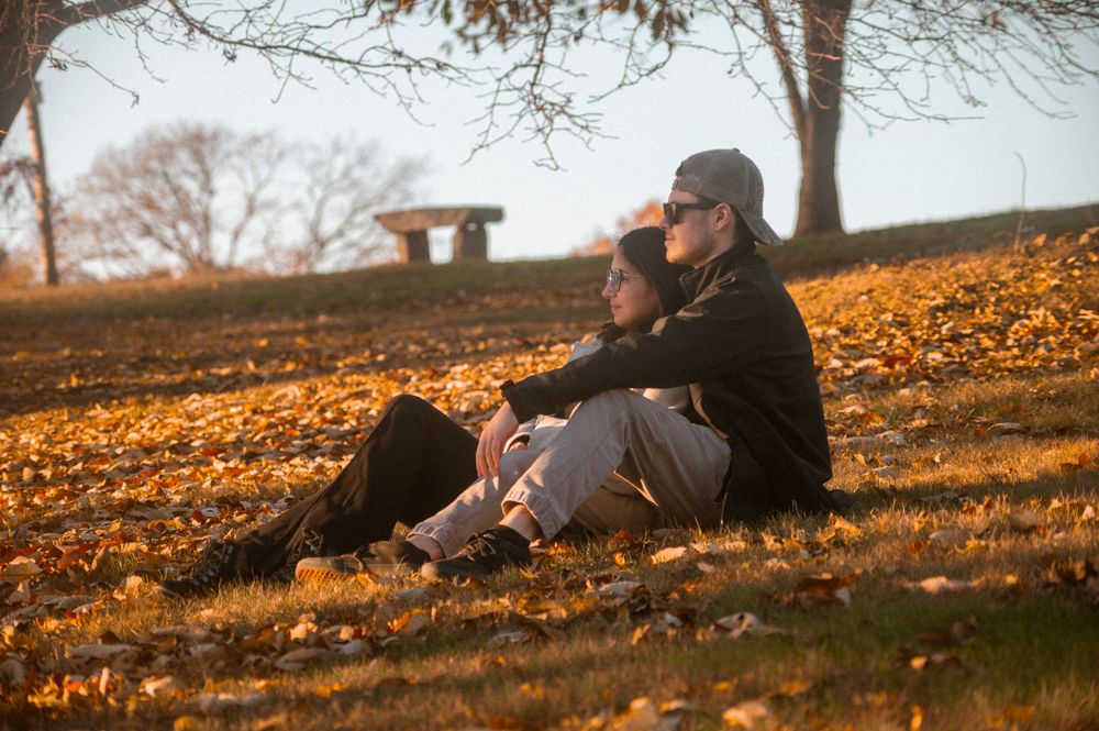 Couple relaxing on autumn ground covered in fallen leaves at sunset.