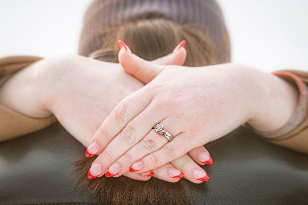 Woman with red nails and diamond ring resting hands on back of head with brown hair.