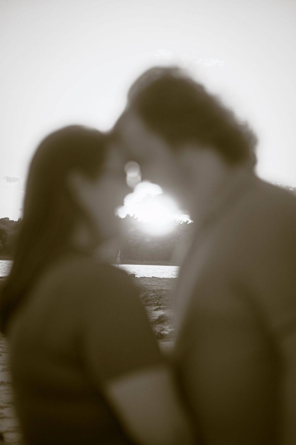 Romantic black and white photo of a couple facing each other with a glowing sunset in the background.