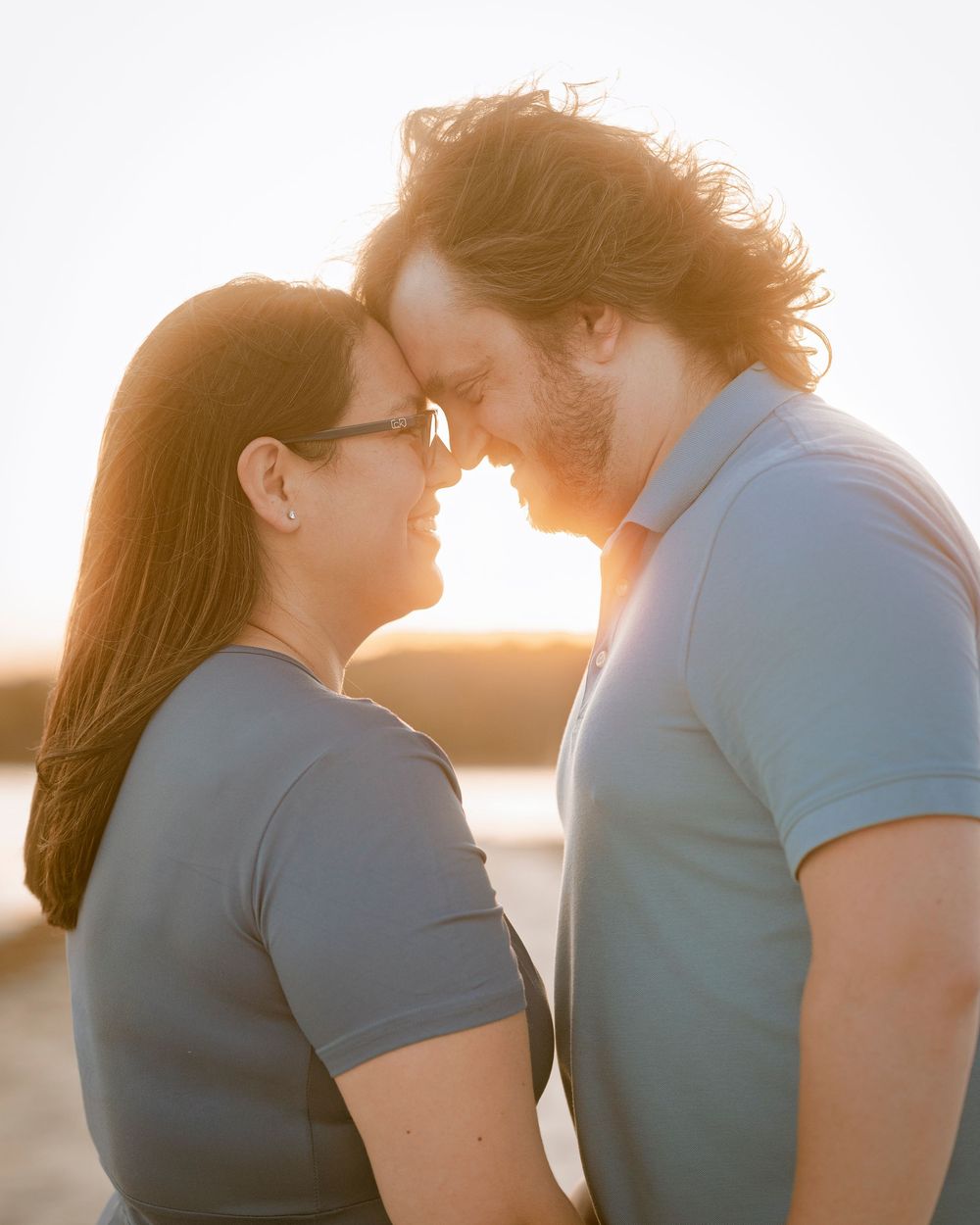 Romantic couple touching foreheads at golden hour sunset, sharing an intimate moment outdoors.