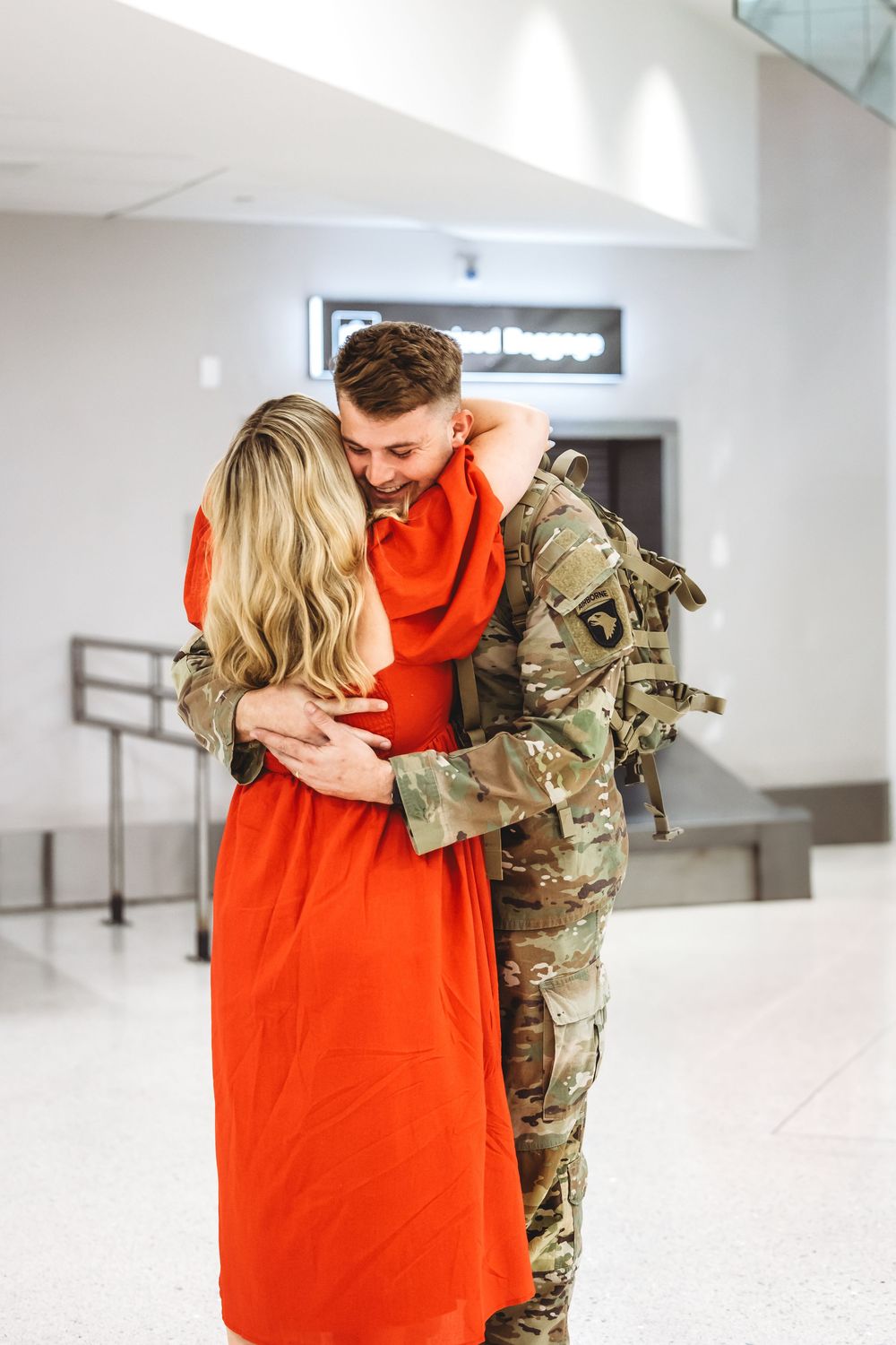 Emotional airport reunion between service member in camouflage and person in red dress in New Haven, CT.