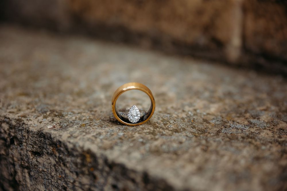 Close-up shot of a gold wedding ring with a diamond on textured stone surface in natural lighting.