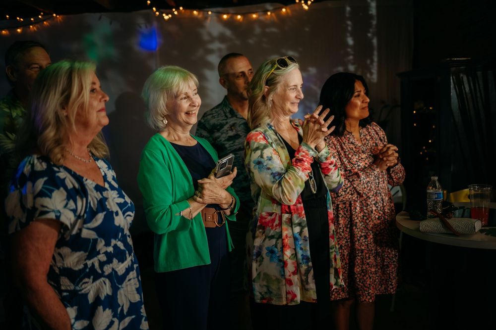 Group of people singing and enjoying themselves at a dimly lit party with string lights in the background.