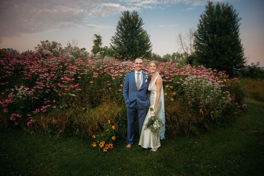 Couple walks together through a beautiful garden filled with blooming pink and orange flowers at sunset.