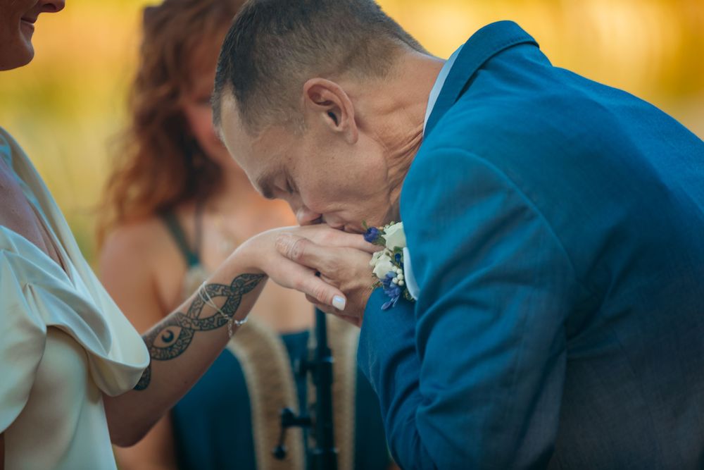 A couple shares an intimate moment during their wedding ceremony, with the groom in a blue suit bowing his head.
