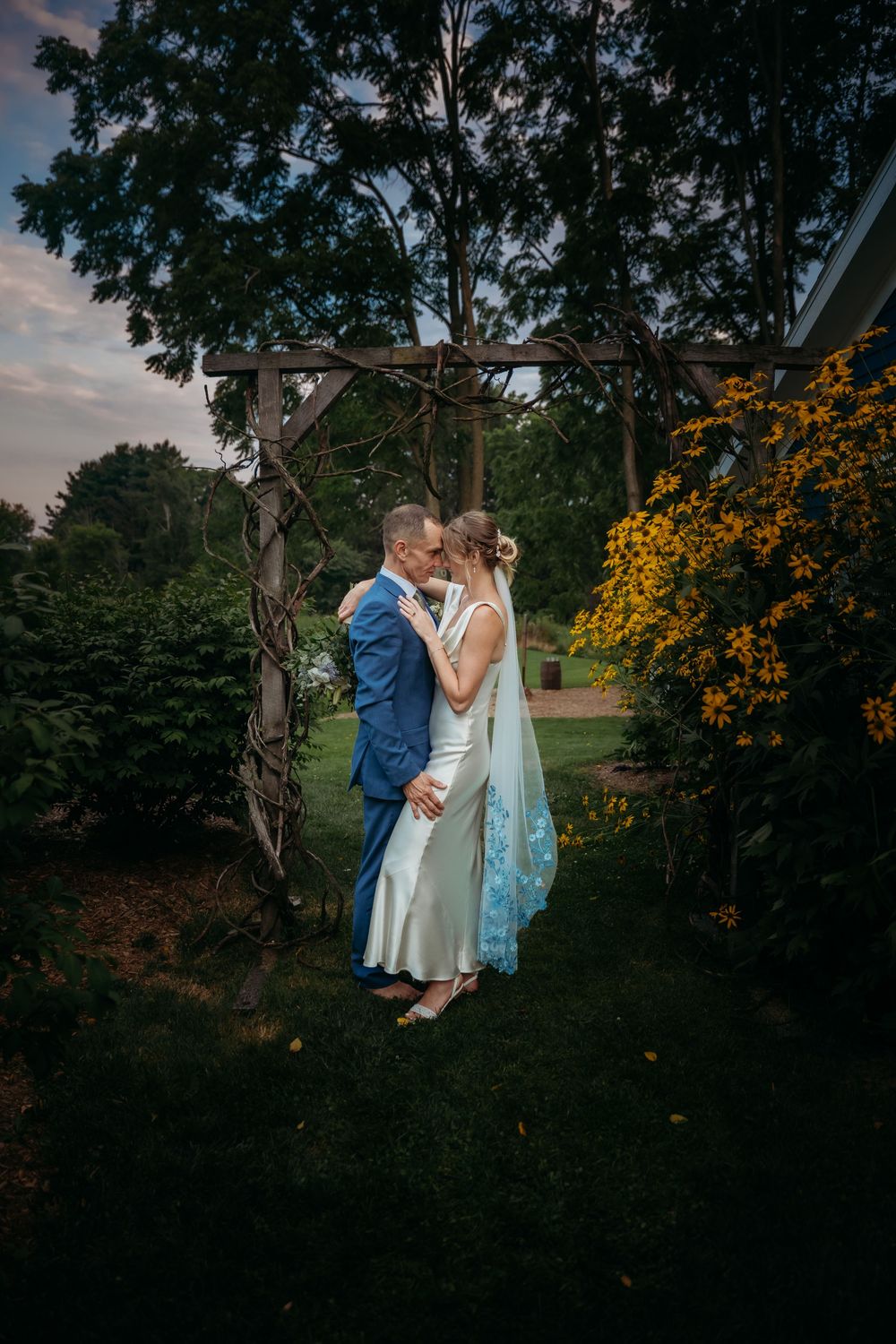 Four romantic outdoor photos showing a couple embracing near a tree with vibrant yellow flowers in a garden setting.