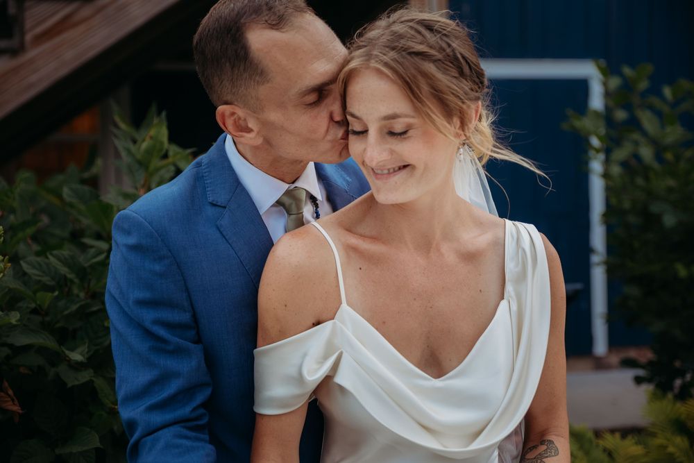 A couple in elegant wedding attire share an intimate moment in a garden setting.