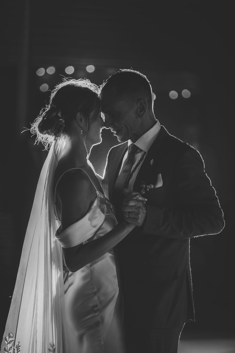 Silhouetted couple embracing in an intimate dance pose against a dark background with soft rim lighting.