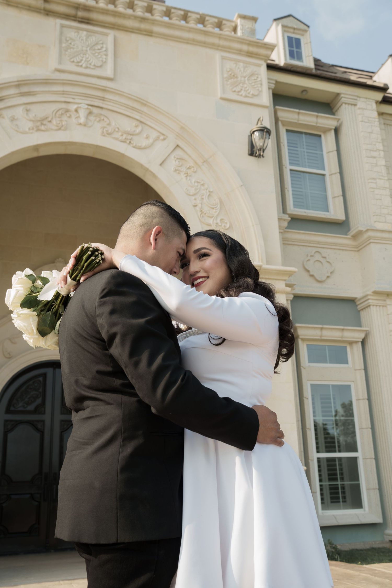 A tender embrace between newlyweds outside an elegant stone building.