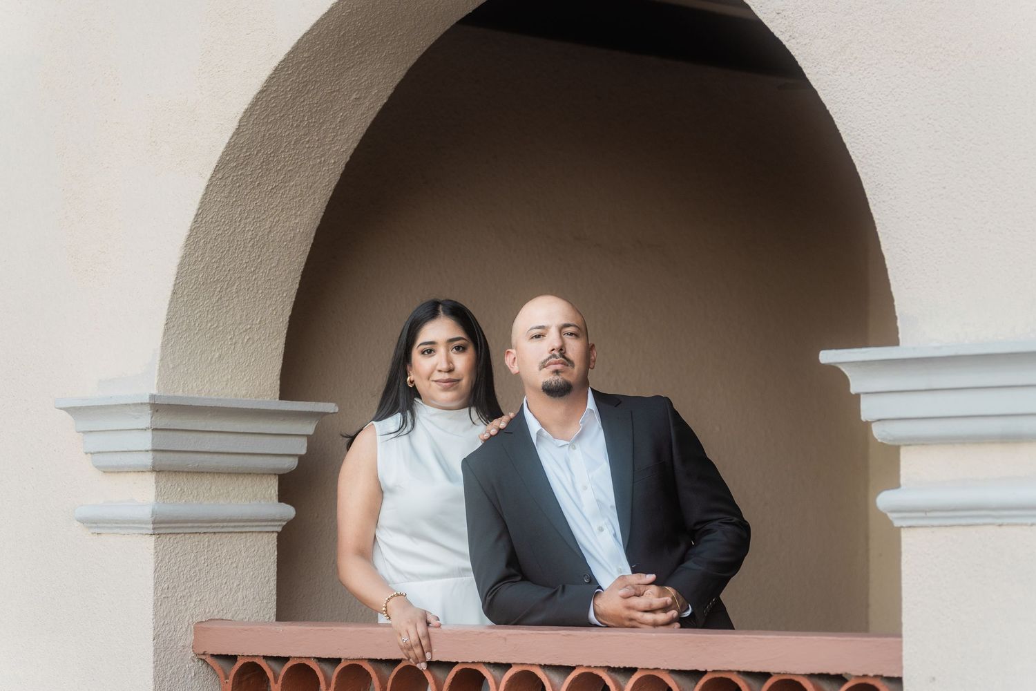 Elegant couple posing under stone archway in formal attire.