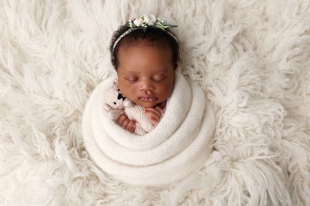 Newborn sleeping peacefully wrapped in white swaddle on fluffy white fur backdrop.