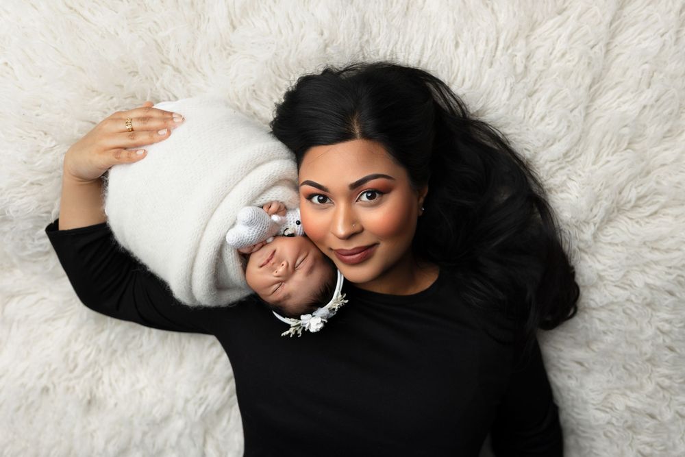 Person in black sweater lying on white fur background holding a small white dog.