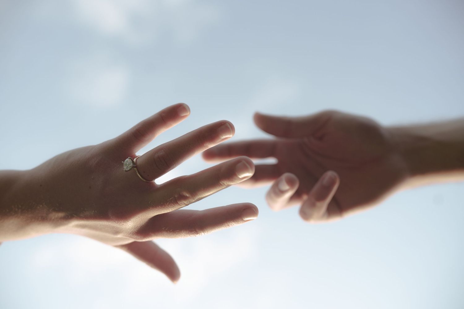 Two hands reaching towards each other against a bright, ethereal background.
