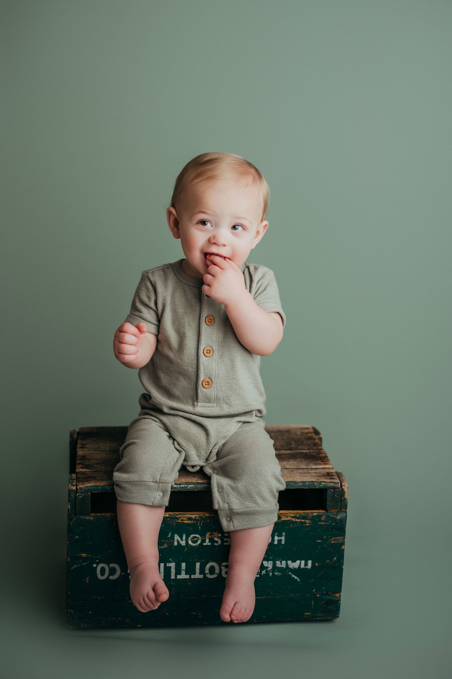 Baby in high chair reaches for white smash cake during first birthday photoshoot.