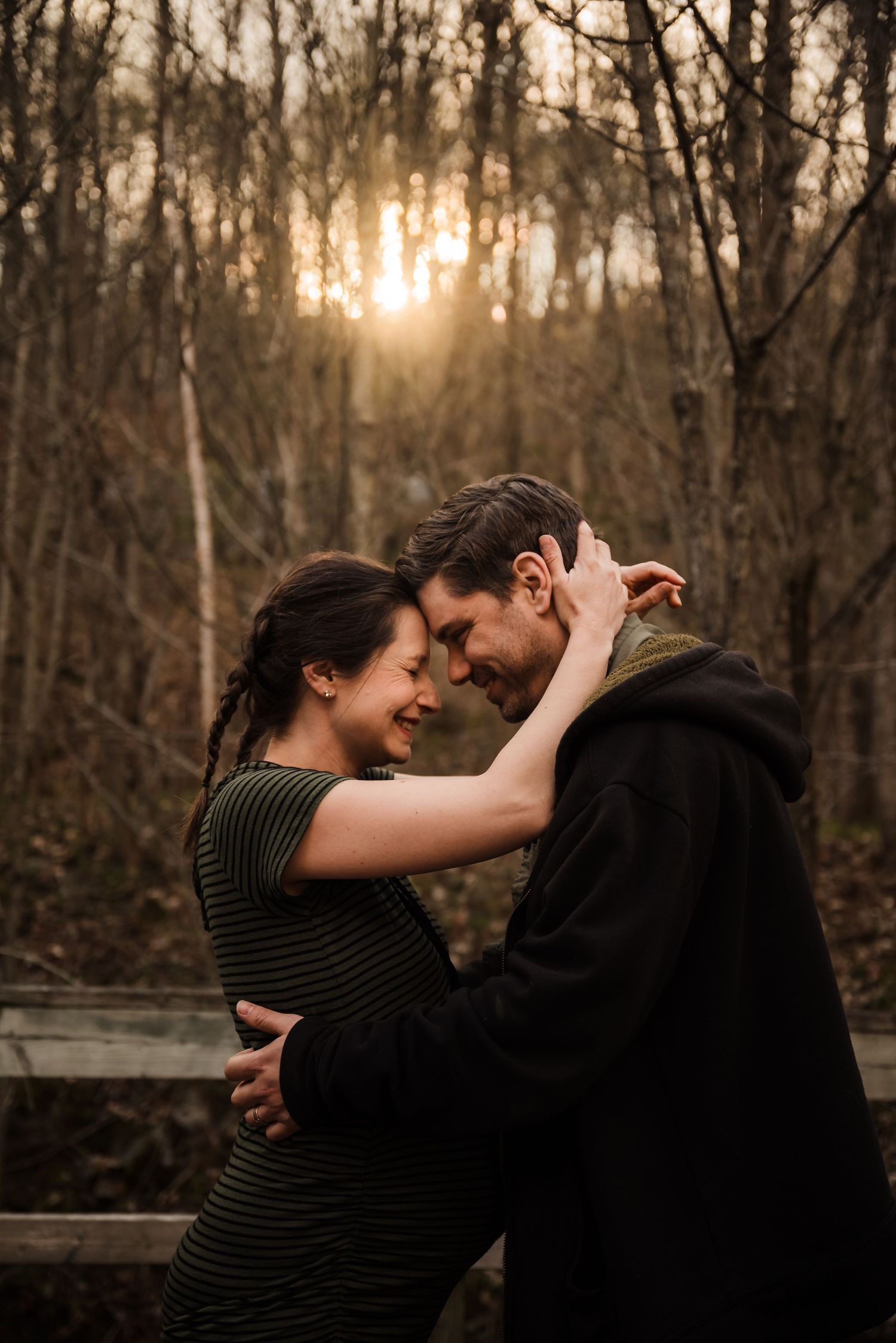 A romantic couple shares an intimate moment in front of a sunset through winter trees.