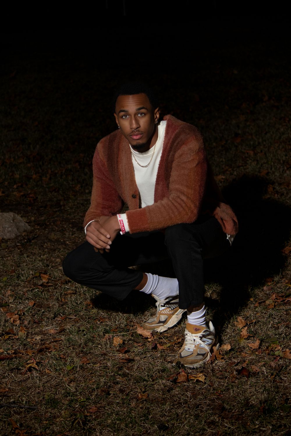 Portrait of person in brown jacket and sneakers sitting on autumn ground at night.