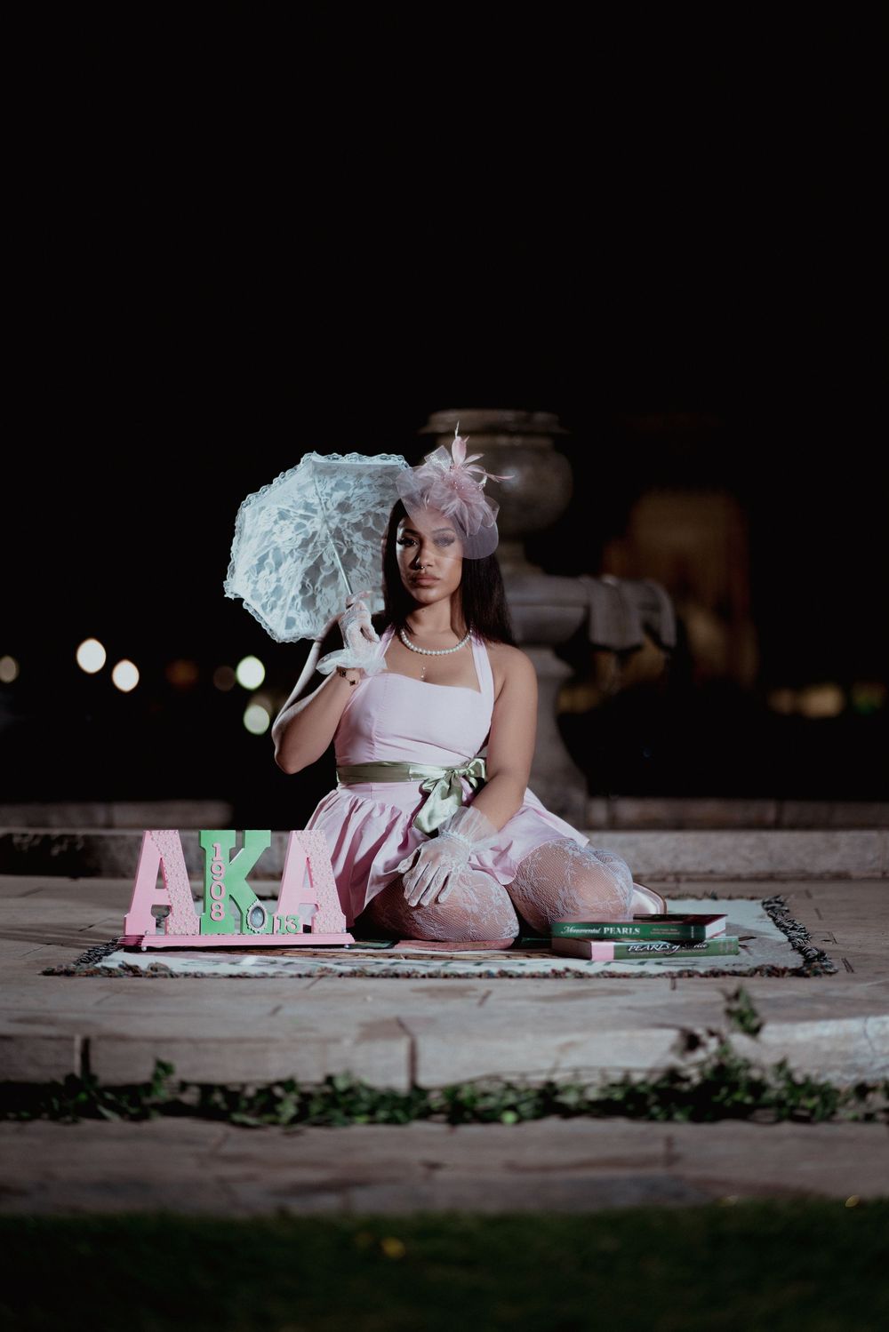 Artistic portrait of someone sitting on ground at night with pink letters and decorative elements in foreground.