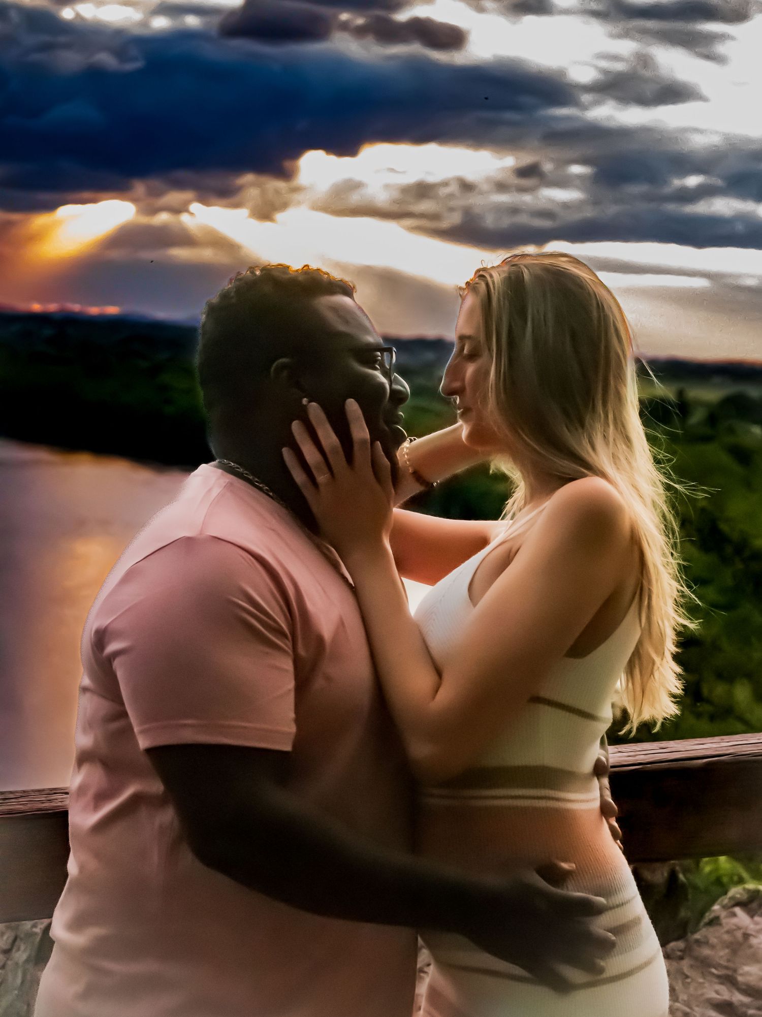 Intimate sunset portrait of a couple embracing on an overlook with dramatic sky.