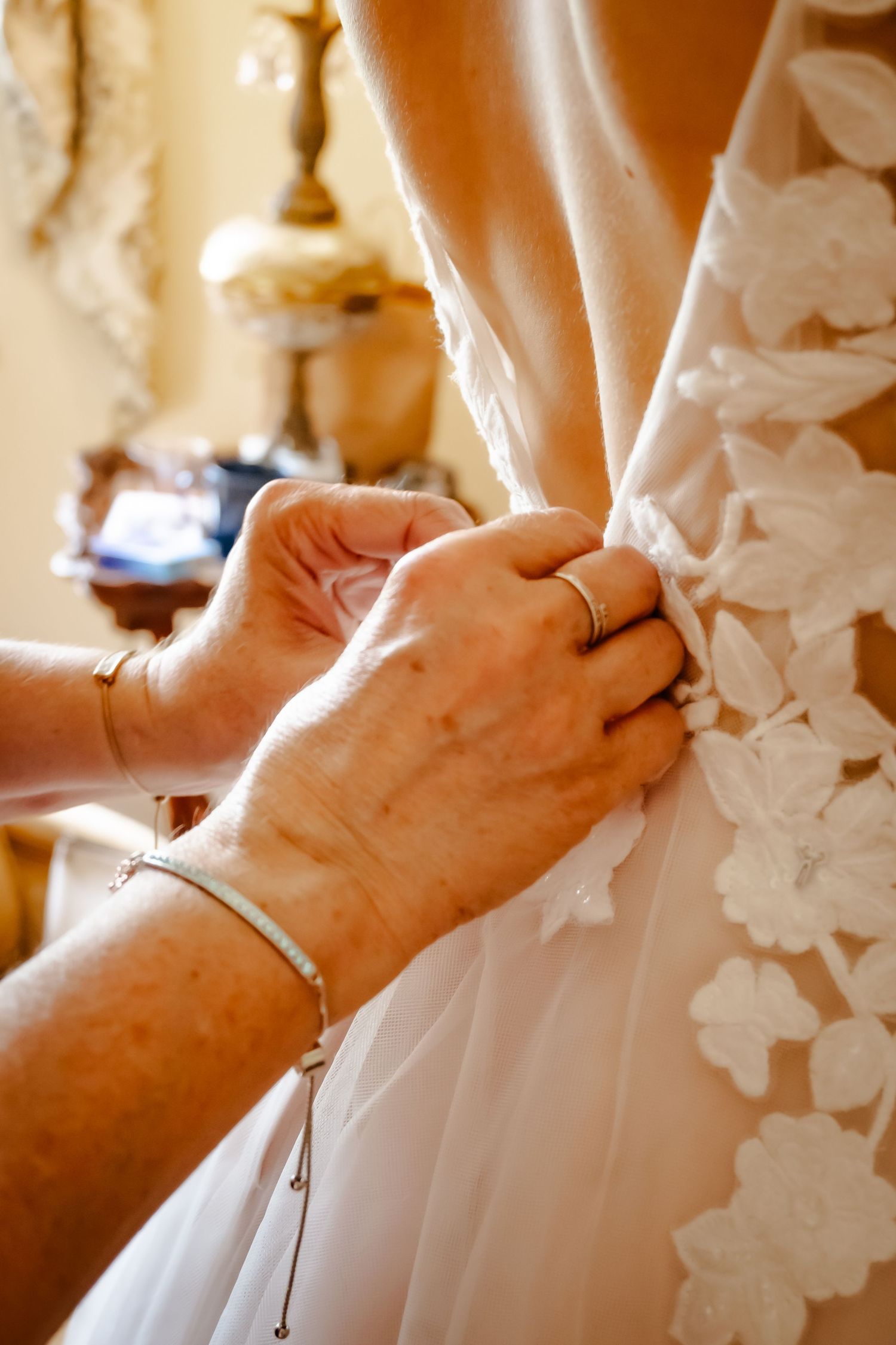 Close-up of hands fastening buttons on a white lace wedding dress.