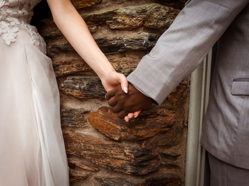 Bride and groom hold hands against a rustic stone wall background.