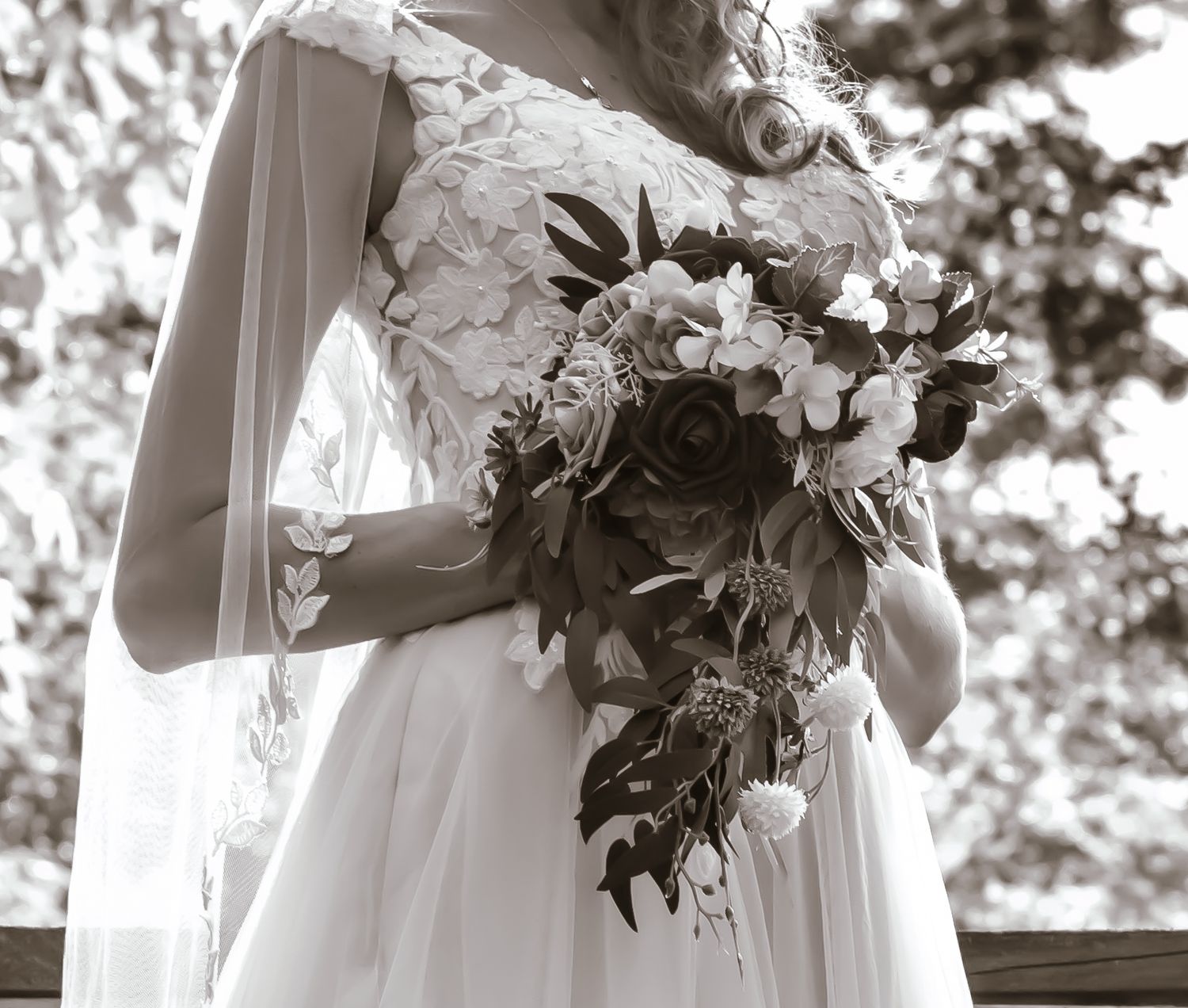 An elegant bridal bouquet with white flowers and greenery held against a flowing wedding dress.