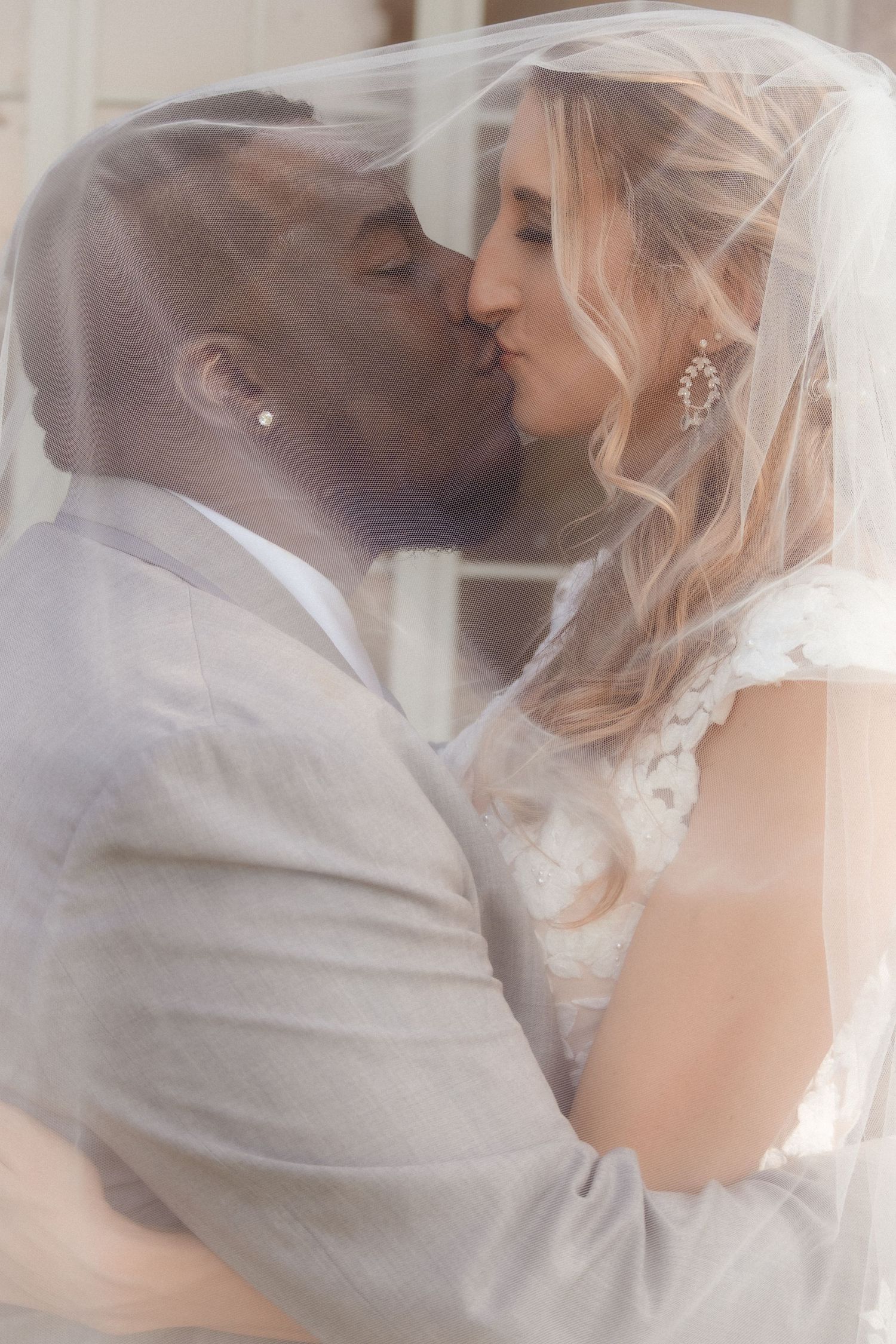 A tender wedding kiss captured under a delicate white veil.