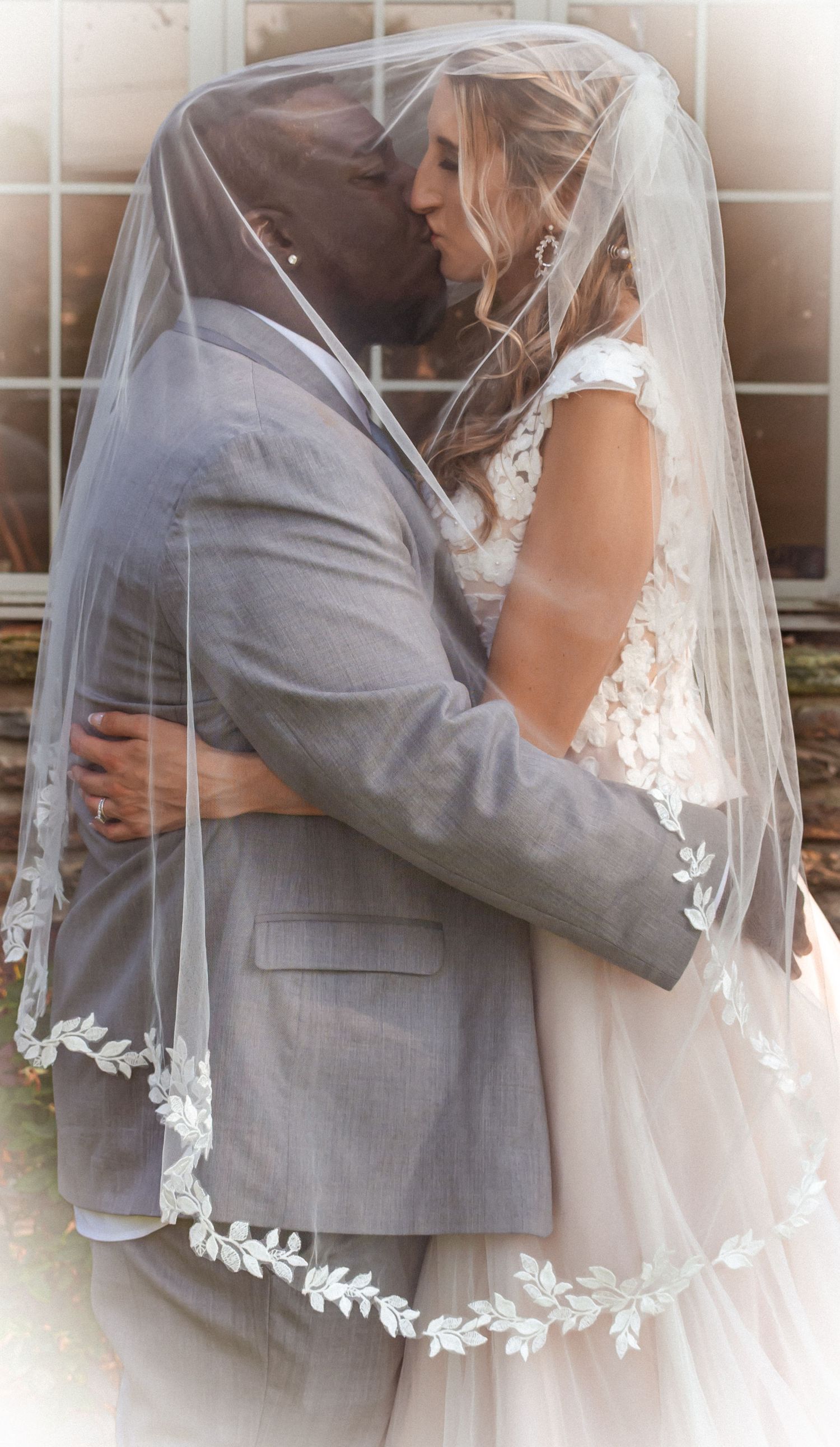 Newlyweds embrace under a flowing lace-trimmed veil.