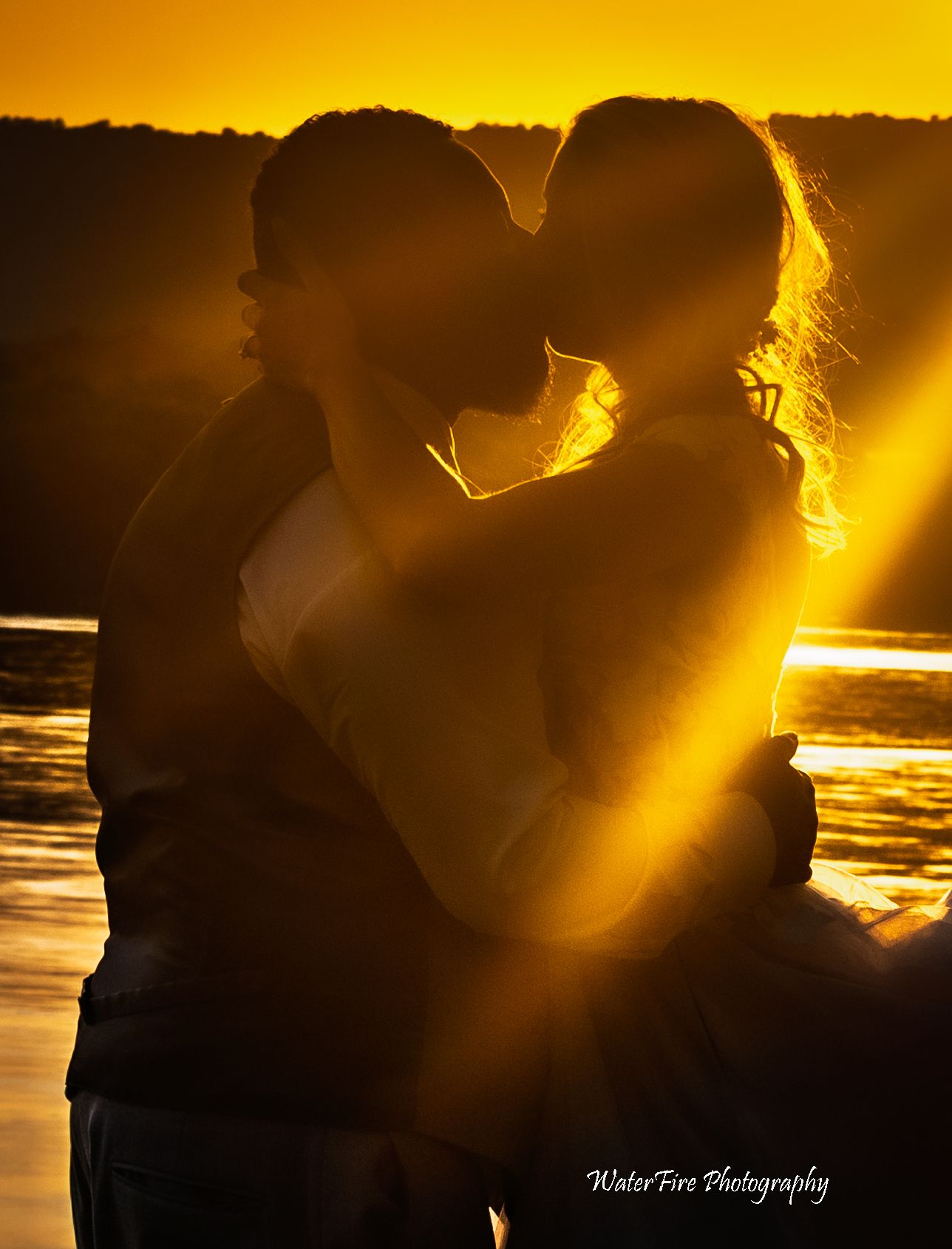 Silhouettes of newlyweds embracing against a golden sunset over water.