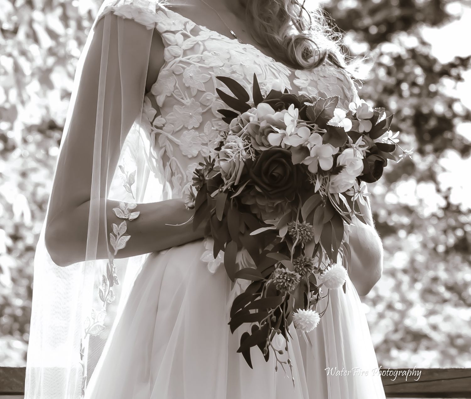 Black and white detail of bridal bouquet with flowing white dress and veil.