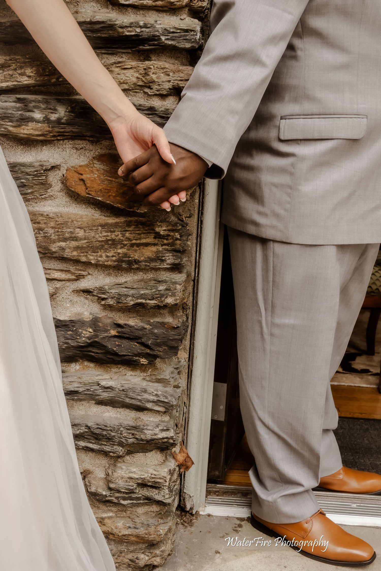 Close-up of couple holding hands against rustic stone wall.