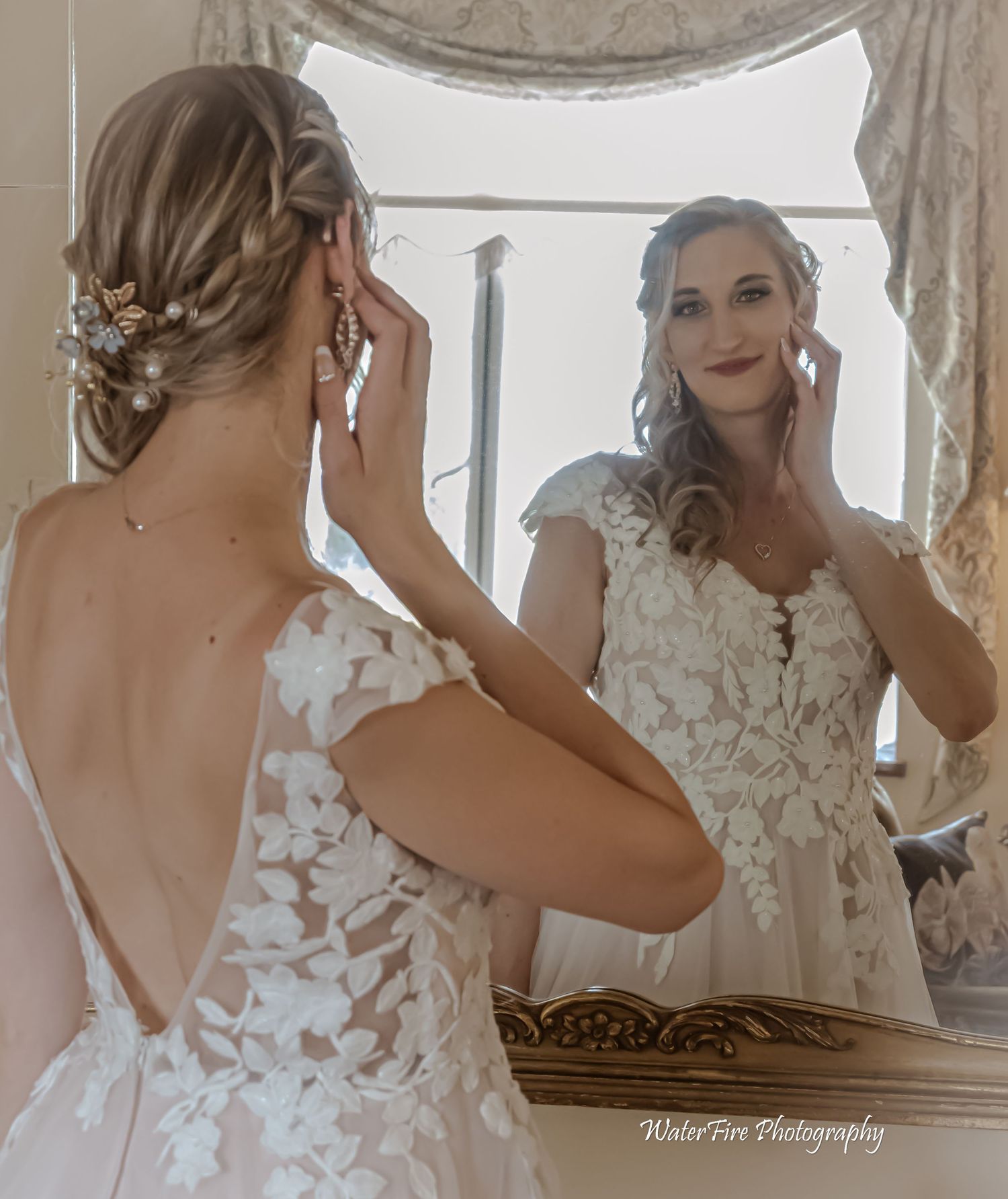 Bride in lace wedding dress looking at reflection in mirror.