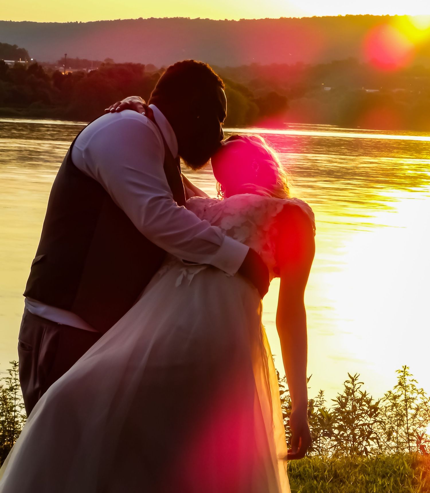 Romantic sunset silhouette of couple embracing by waterfront.