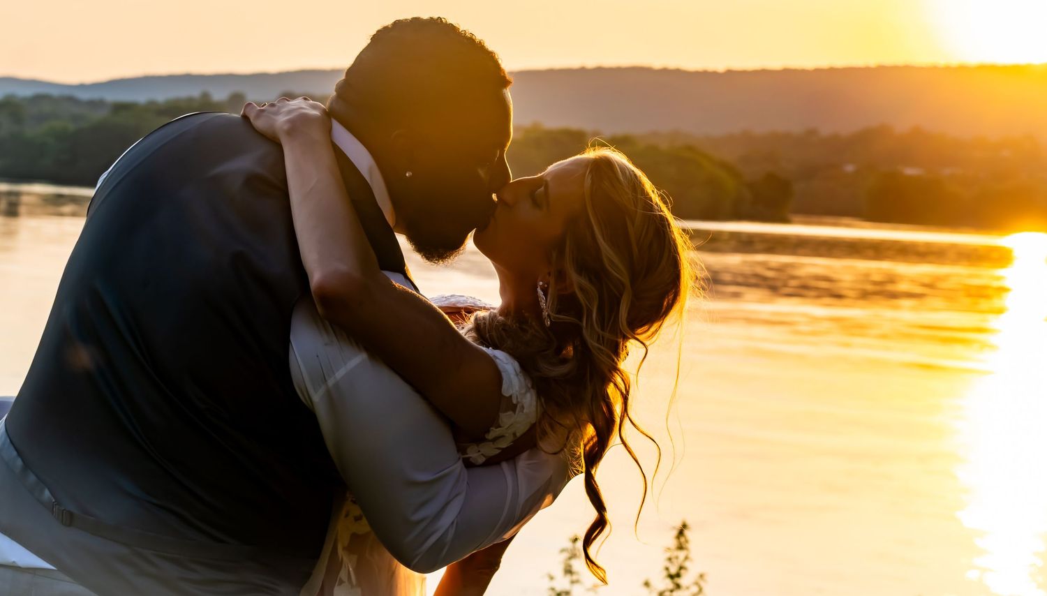 A romantic silhouette of a couple embracing at sunset by a tranquil lake.
