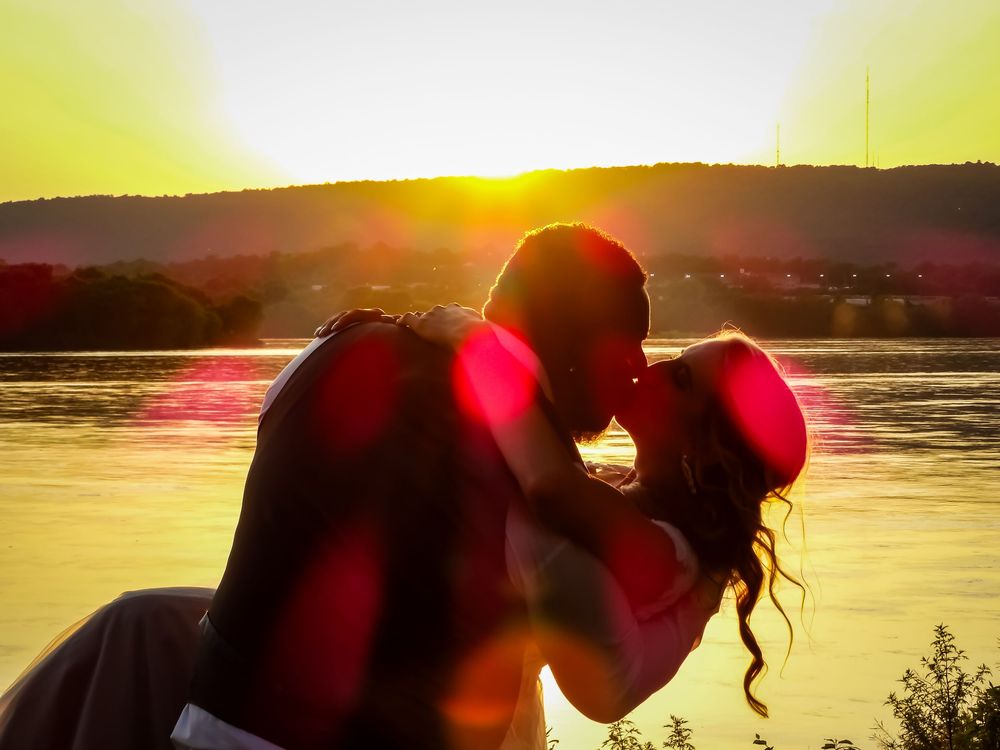 Dramatic sunset silhouette with couple embracing against water backdrop.
