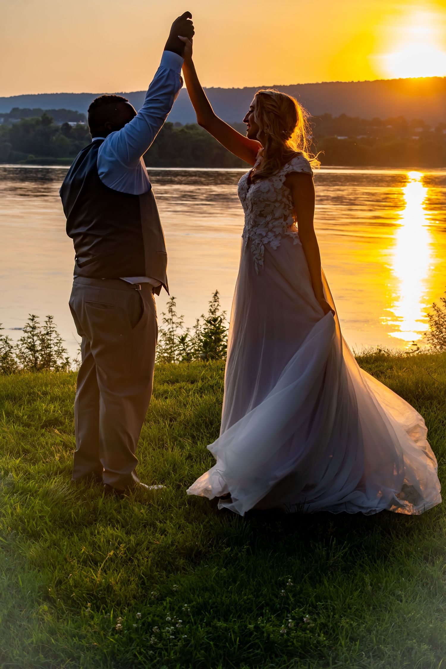 Bride and groom give high five at sunset overlooking a serene lake.
