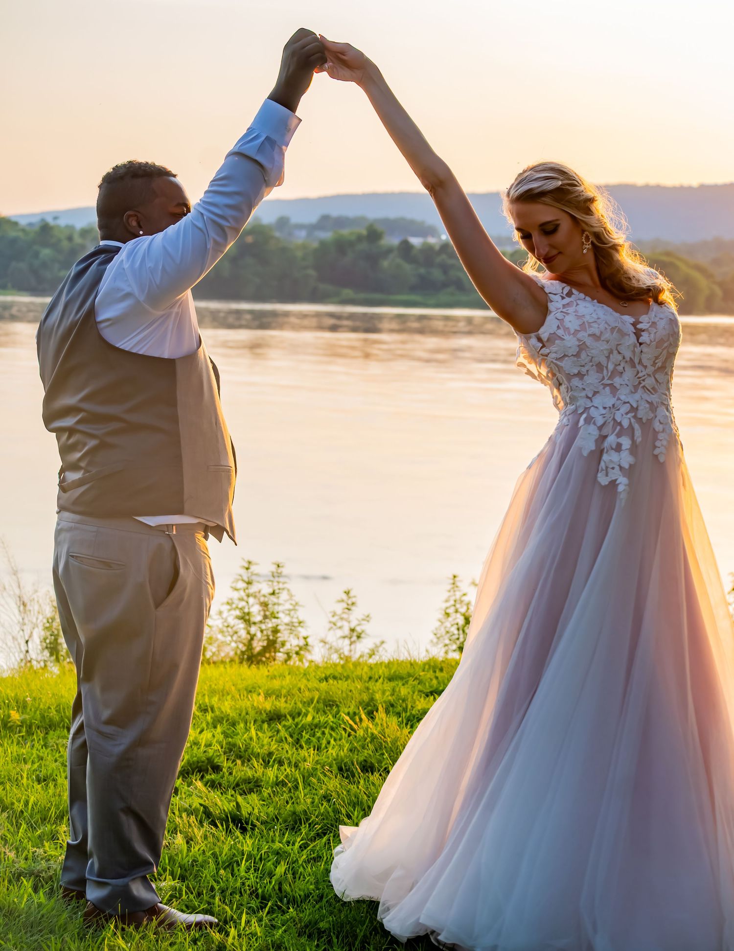 Dance pose silhouetted against sunset lake with bride's flowing gown.