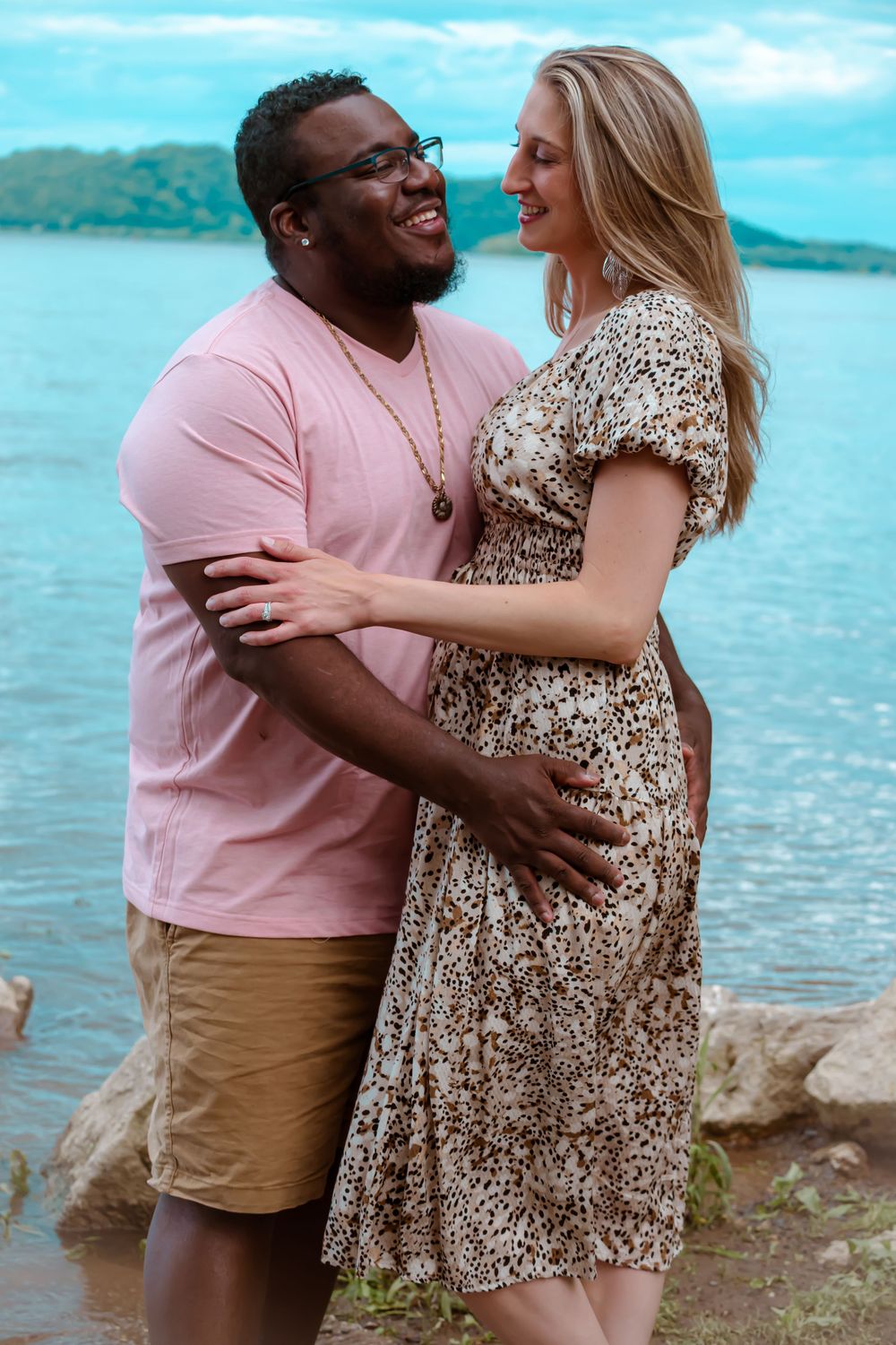 A romantic couple embraces near the water, wearing coordinating pink and floral outfits.