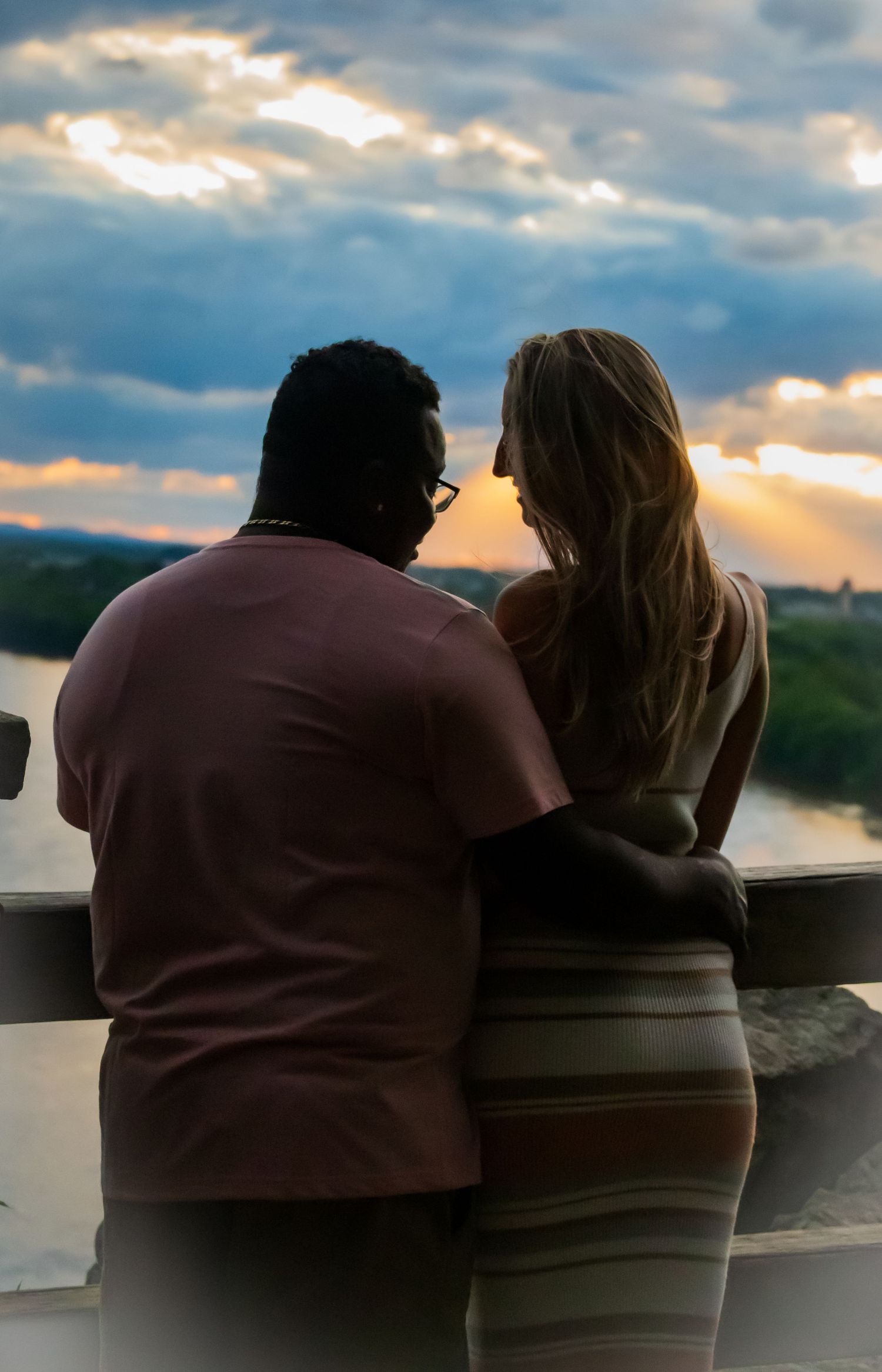 A couple watches the sunset together, silhouetted against dramatic cloudy skies.