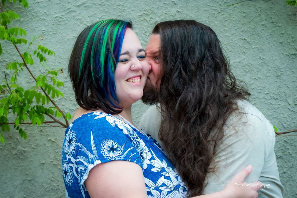 Two people share an intimate moment together while embracing outdoors against a textured wall.