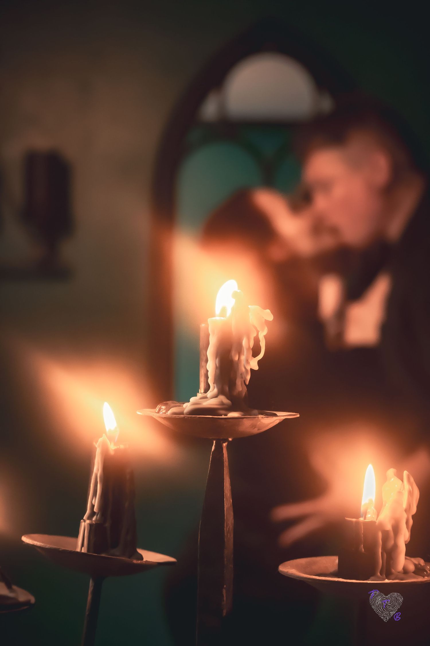 Three lit candles in ornate holders glow warmly in the foreground as a blurred figure prays in a dimly lit chapel.