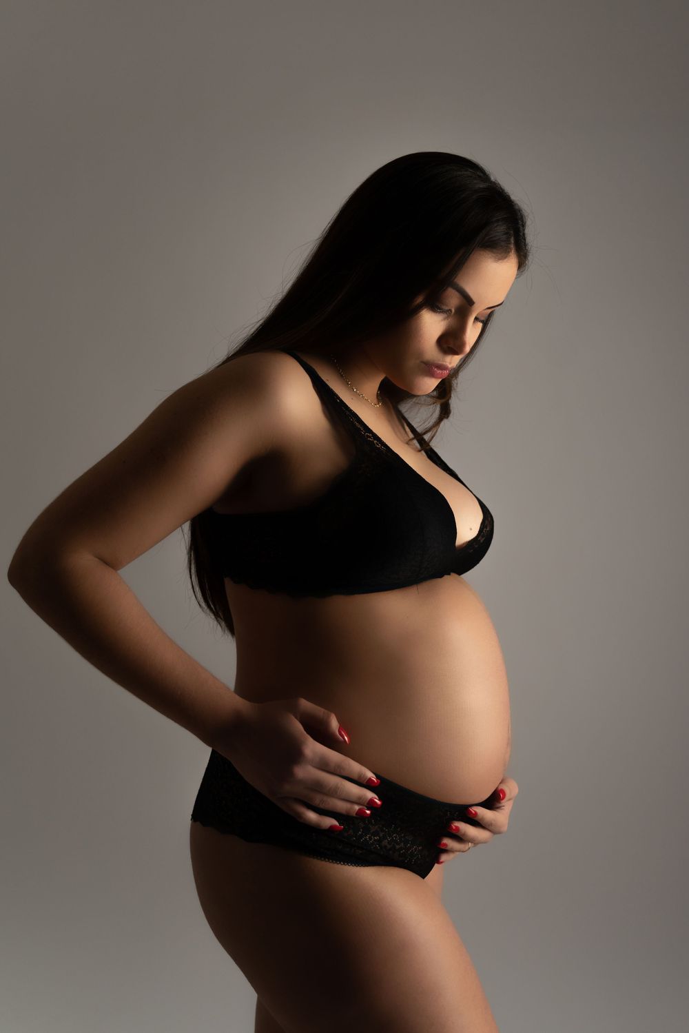 Artistic maternity portrait in black lingerie against gray background.