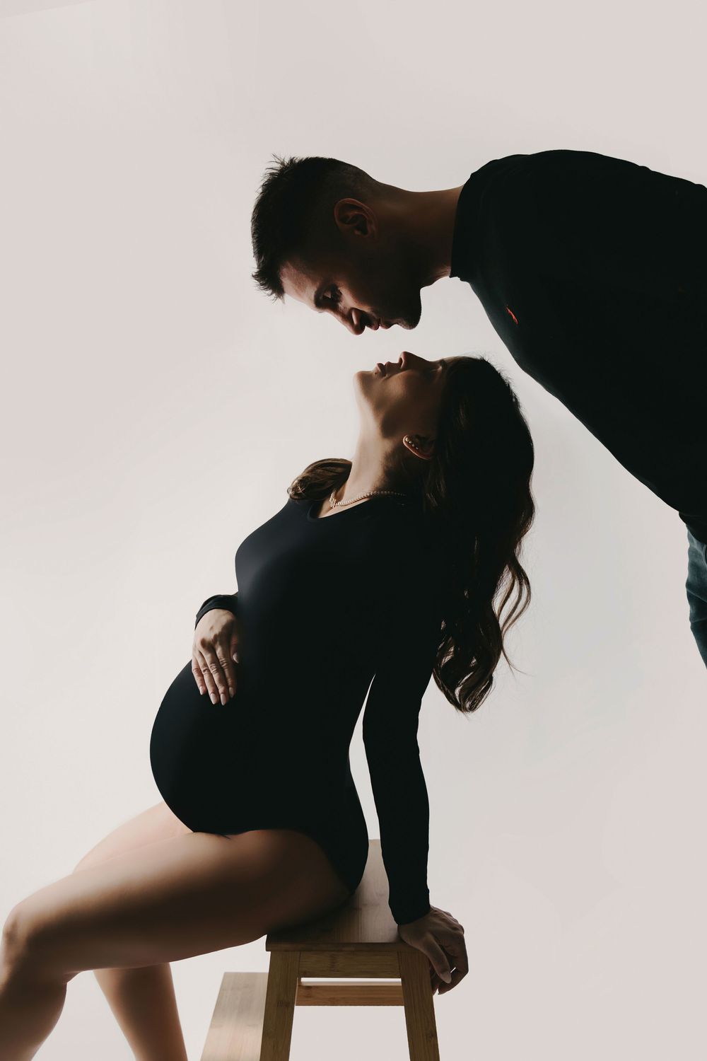 Silhouette of a couple in a romantic pose against white background with person sitting on wooden stool.