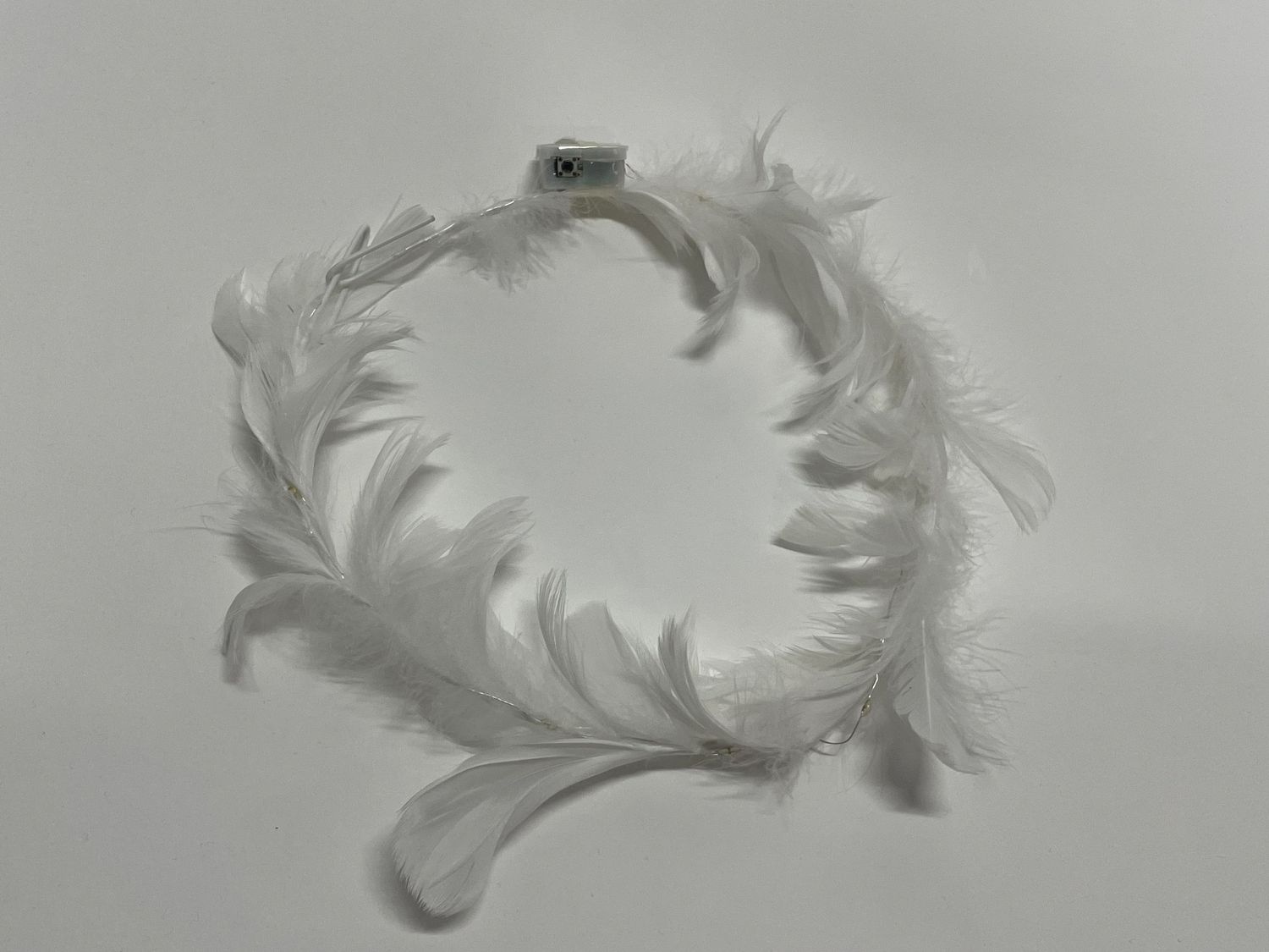 White feather crown arranged in a heart shape on gray background.