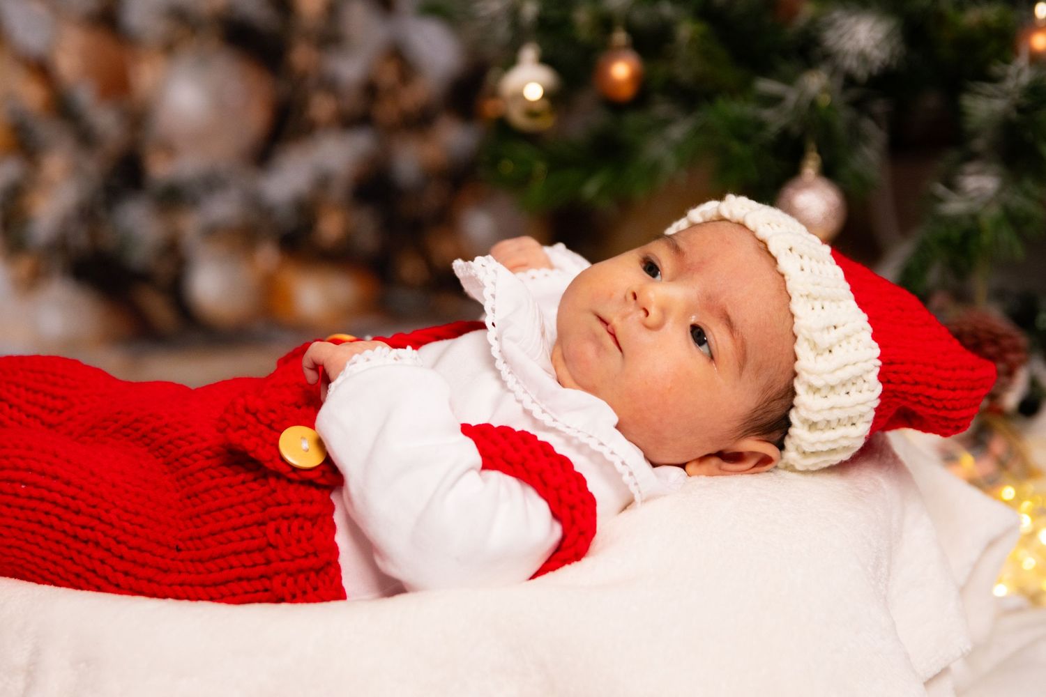 Newborn baby sleeping on red blanket with Christmas decorations in background.