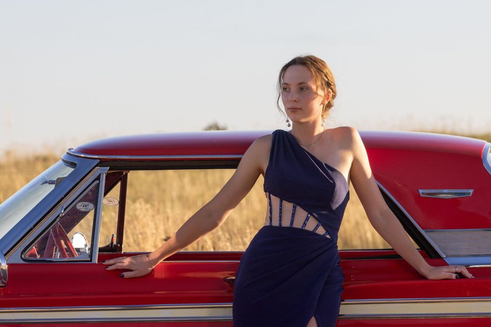Classic red car paired with elegant Navy blue dress in rural setting.