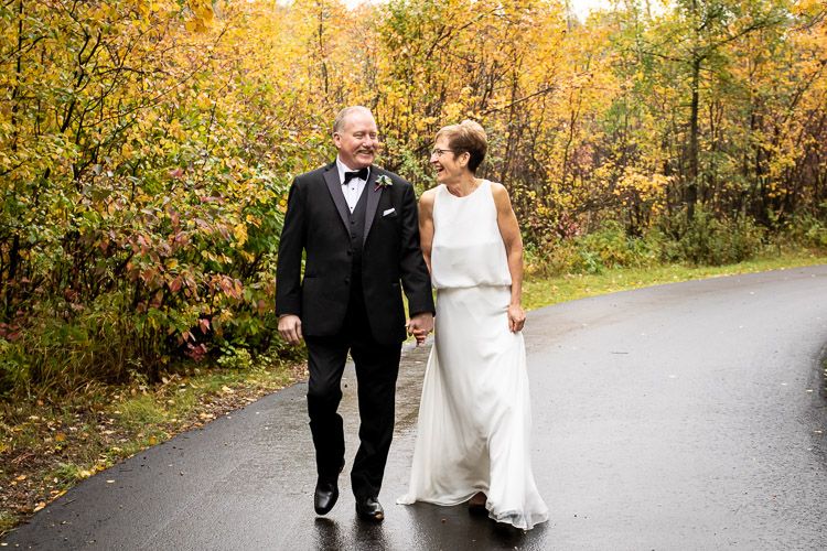 A couple walks hand in hand along an autumn path surrounded by golden foliage.